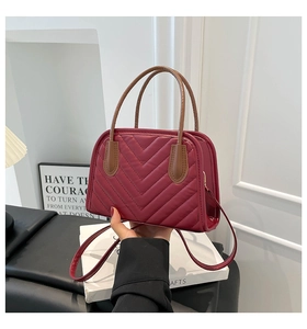 Close-up of wine red quilted handbag with V-shaped stitching and brown top handle