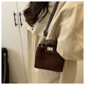 Detail of dark brown tote bag with suede texture and gold twist lock on trench coat