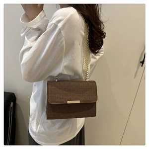 Détail du sac bandoulière marron foncé avec texture tressée et chaîne dorée