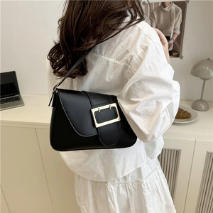 Minimalist black leather baguette bag with a striking gold buckle on a shoulder strap