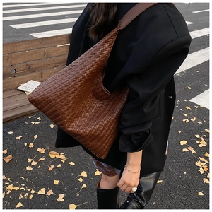 Detail of a dark brown woven leather hobo bag showing the intrecciato pattern in autumn light