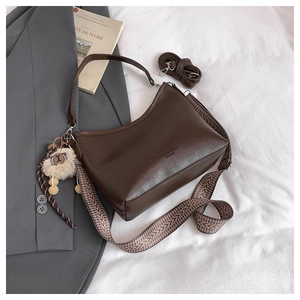 Détails d'un sac marron foncé avec sangle à motifs, lettrage mode et pompon en peluche