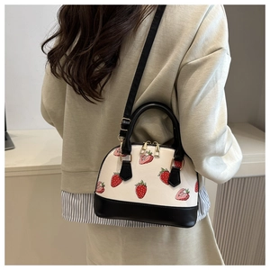 Détail du sac en forme de coquillage avec imprimés fraises et poignées en cuir noir