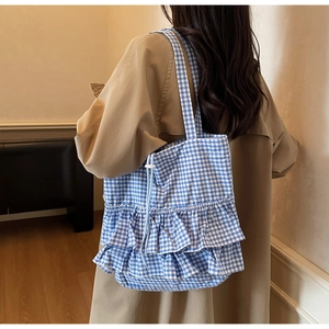 Detailed blue and white checkered tote bag with ruffle trim on model in trench coat