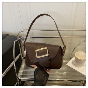 Detail of dark brown baguette bag with golden square buckle on a silver shelf