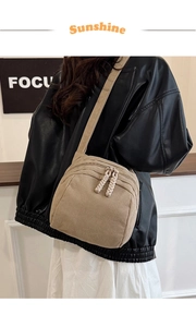 Detail of beige corduroy shell bag with dual zippers and woven pulls on a wide strap