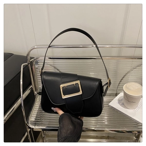 Detailed view of black leather shoulder bag with vintage gold square buckle on a shelf