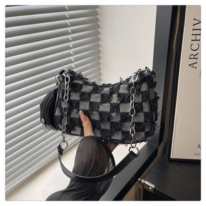Detail of checkered shoulder bag with distressed frayed edges and silver chain strap