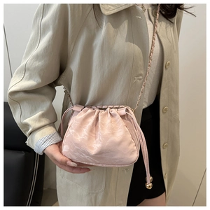 Pink drawstring cloud bag with gold chain strap shown on a beige trench coat