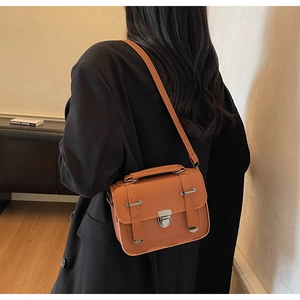 Close-up of a vintage brown leather messenger bag with metal buckles on a black coat