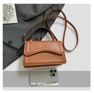 Close-up of caramel leather crossbody bag with curved stitching and smartphone for size