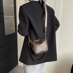 Sac seau rétro marron avec bandoulière tissée large et logo doré porté par un mannequin