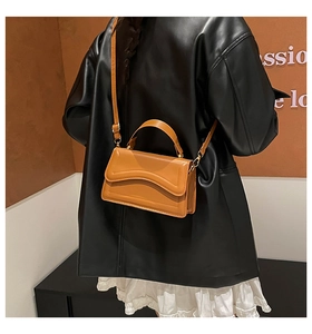 Caramel brown handbag with wave flap and adjustable strap shown on model over shoulder