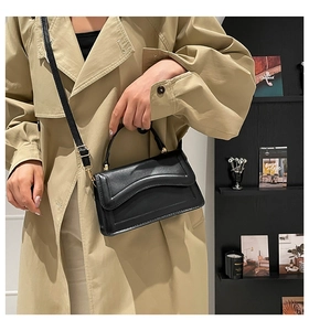 Detail of a luxury black leather crossbody bag paired with an elegant beige trench coat