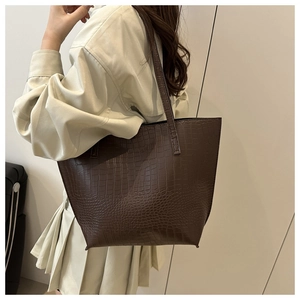 Side view of a dark brown crocodile texture tote bag worn over the shoulder by a model