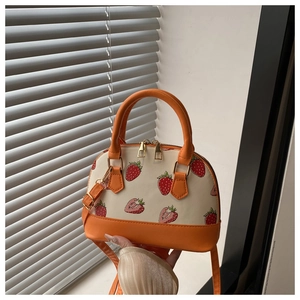 Detail of strawberry print strawberry shell bag with orange handles and gold zippers
