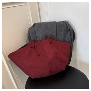 Close-up of wine red matte suede tote bag with knotted handle detail on grey coat background
