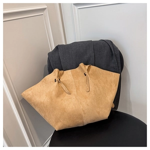 Detail view of khaki suede tote bag featuring winged design on a black leather chair