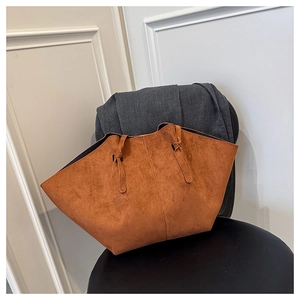 Close-up of caramel suede wing tote bag with knot straps on a black stool
