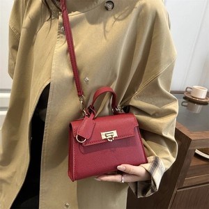 Deep red leather mini handbag with gold hardware worn over a beige trench coat