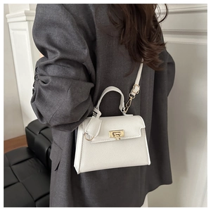 Detail van een witte crossbodytas met gouden slot gedragen op een grijze blazer
