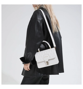 Detail view of a white quilted crossbody bag with gold buckle and top handle worn by model