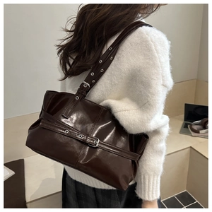 Detail of dark brown glossy PU leather tote bag with silver buckle on model shoulder