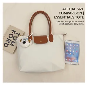 Vue détaillée du sac cabas en toile blanche avec anses en cuir brun et breloque chien