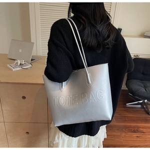 Detailed view of silver large capacity tote bag with embossed lettering on model shoulder