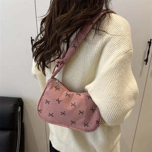 Pink corduroy shoulder bag with black bow patterns shown on a model in a cozy setting