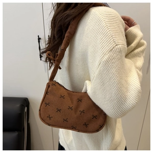 Detail shot of brown corduroy shoulder bag featuring black bow prints and knot strap
