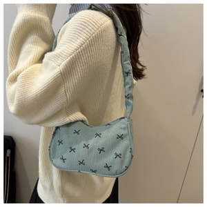 Detail of light blue corduroy shoulder bag with black bow print and textured finish