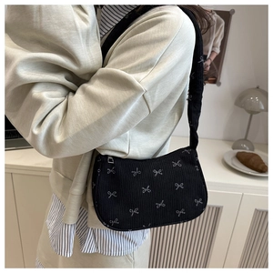 Detail of black corduroy shoulder bag with white bow print and zipper on a model