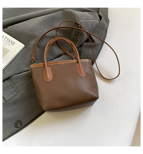 Detail of brown pebble leather bucket bag with adjustable strap on a grey blazer