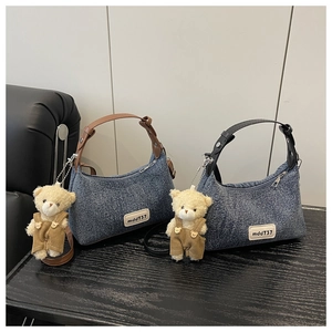 Detail of vintage denim crossbody bag with plush bear charm and metallic text patch