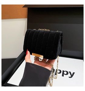 Detail of black velvet crossbody bag with quilted texture and golden chain strap