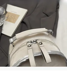 Detail of white leather backpack with dual zippers, silver trim and reinforced handle