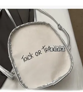Detail view of white crossbody bag featuring silver trim and Trick or Treat typography