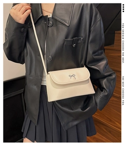 Détail d'un sac bandoulière crème avec nœud en métal porté par un mannequin en intérieur