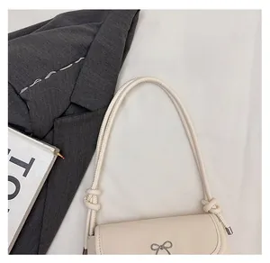 Détail d'un sac à main beige avec poignée tressée et décoration de nœud argenté