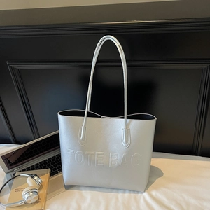 Metallic silver large tote bag with embossed letters on a white bed background
