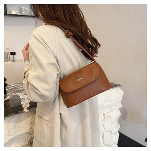 Gros plan sur sac bandoulière en cuir marron avec nœud argenté et détails de sangle noués