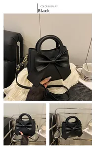 Detail of elegant black PU leather handbag with large bow decoration and slim strap