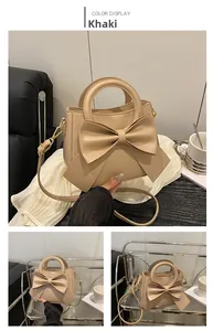 Close-up of khaki handbag featuring a large bow decorative detail and gold metal hooks