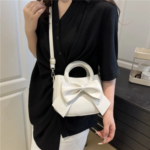 White faux leather crossbody bag with oversized bow design worn by a female model