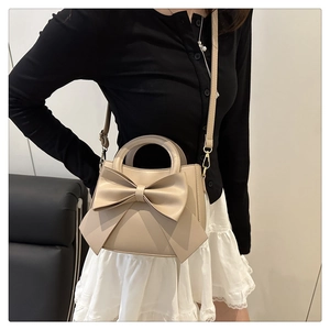 Detail of a beige trapezoid handbag with a large bow and gold-tone metal hooks