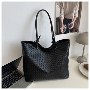 Close-up of the woven texture on a black tote bag with slender knotted shoulder straps