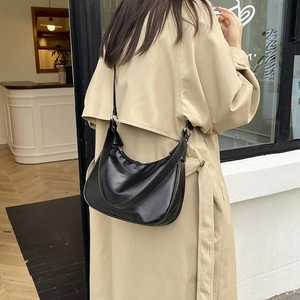 Sac hobo minimaliste en cuir noir mat pour femme porté avec un trench-coat beige élégant