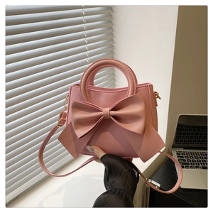 Detail of light pink faux leather handbag featuring a large bow and round handle