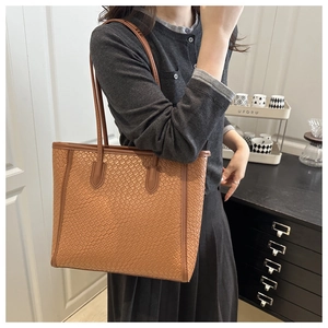 Close-up of caramel brown tote bag featuring intricate woven texture and leather handles